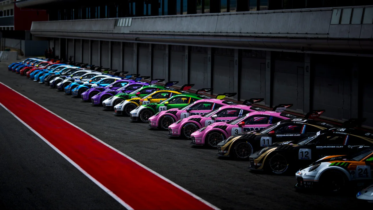 Rząd kolorowych samochodów Porsche 911 Cup w alei serwisowej w Monako, zaparkowanych obok siebie pod ciemnym garażem.