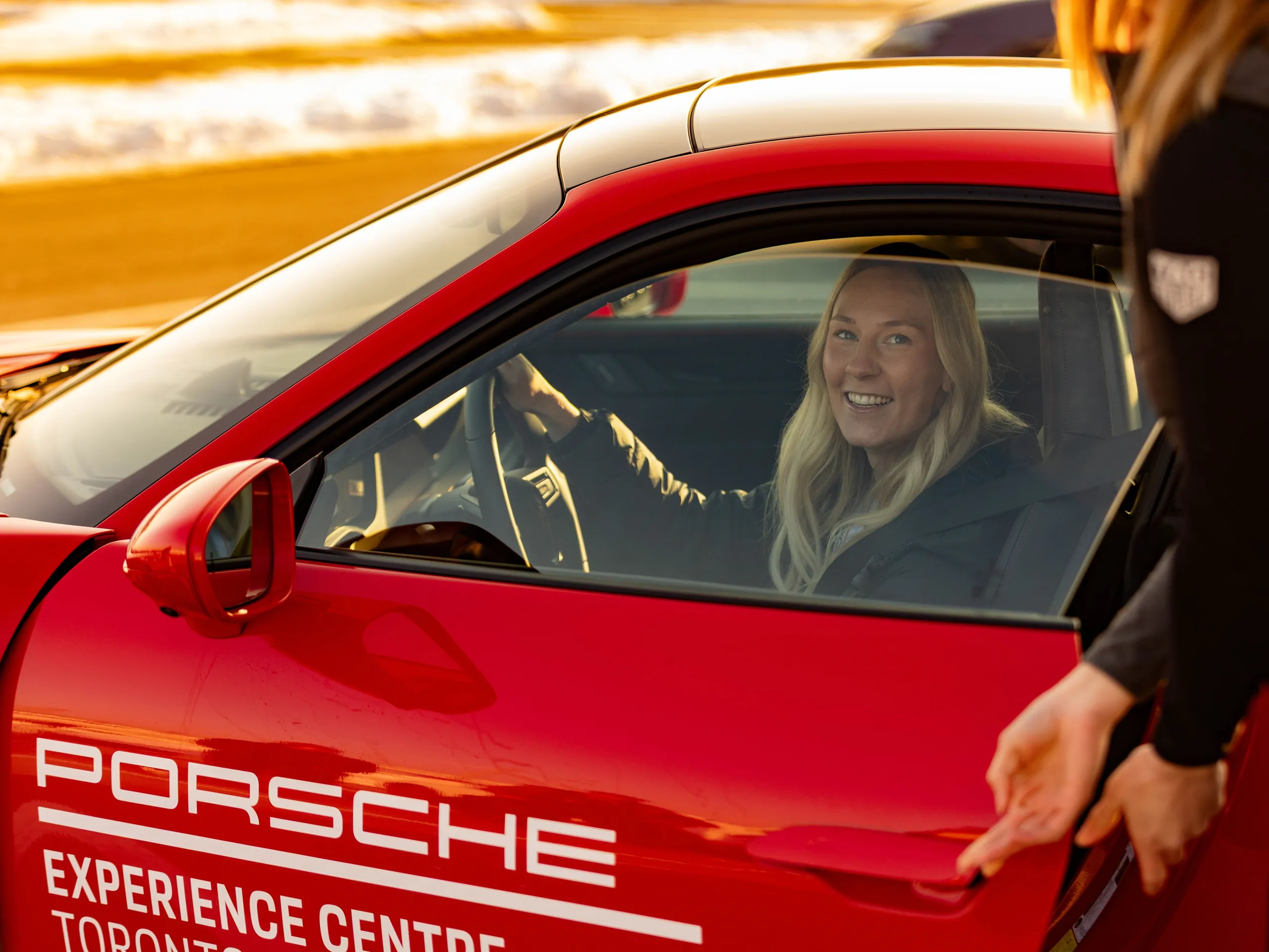 A woman sitting in a red Porsche with an instructor.