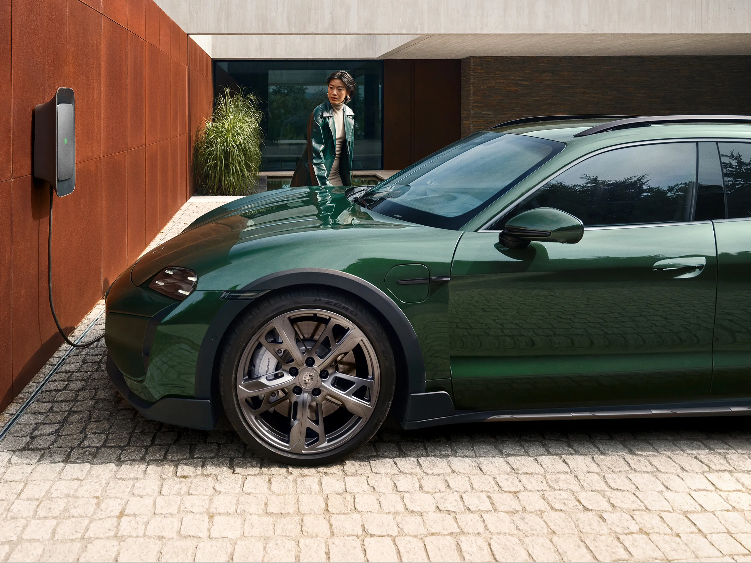 Person charges a green Porsche at a wallbox in front of a modern home.
