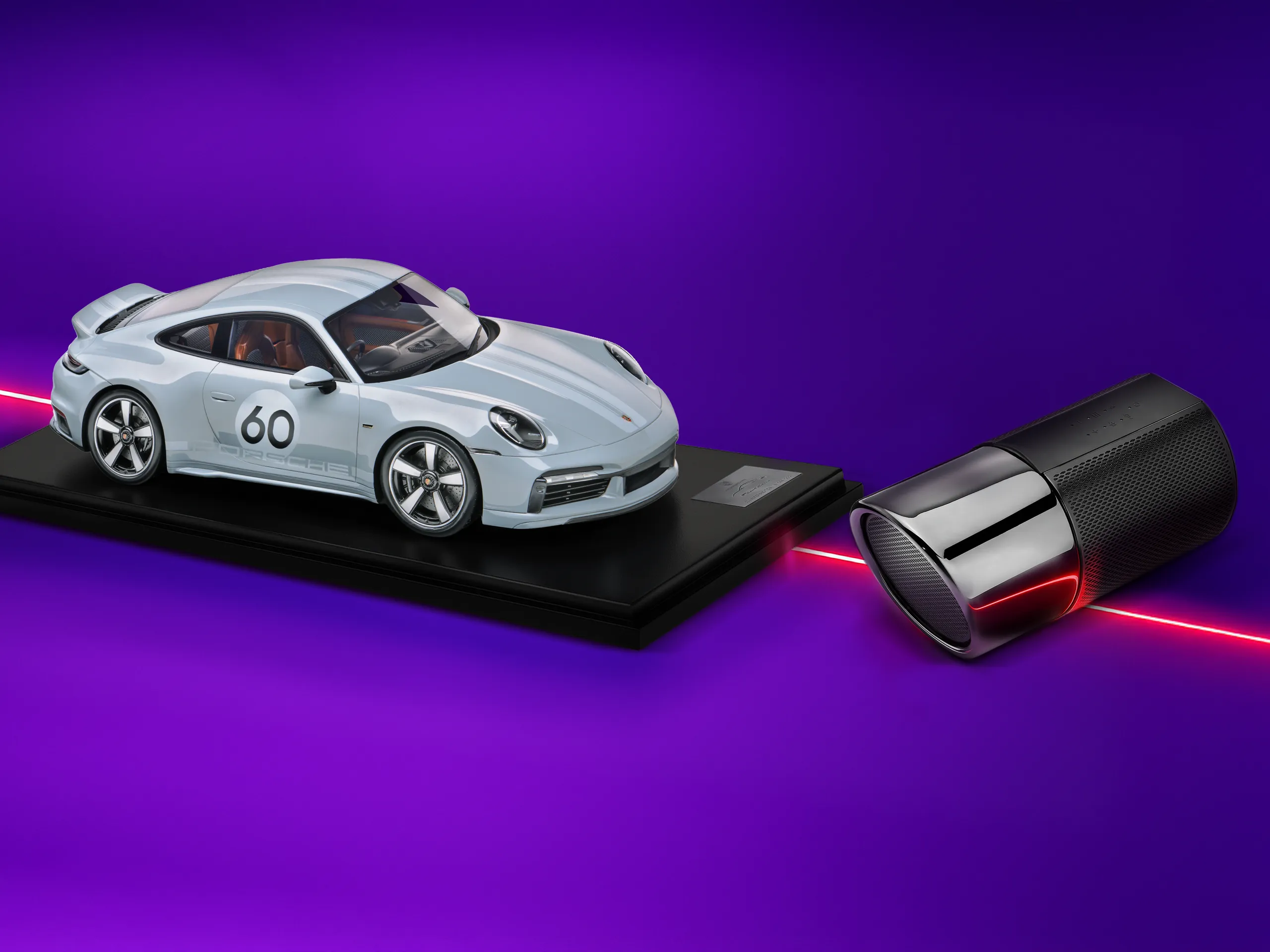 Une voiture miniature Porsche et une enceinte posées sur un fond violet vif avec un éclairage néon.