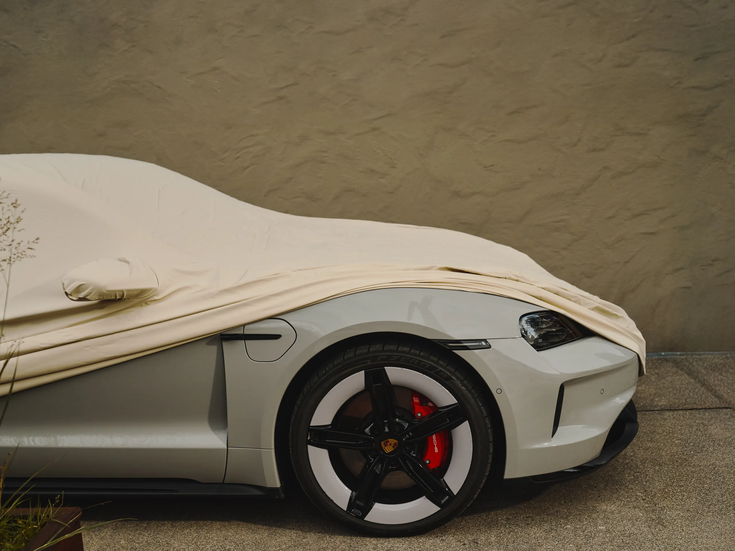 A side shot of a white Taycan partially covered by a car cover. 