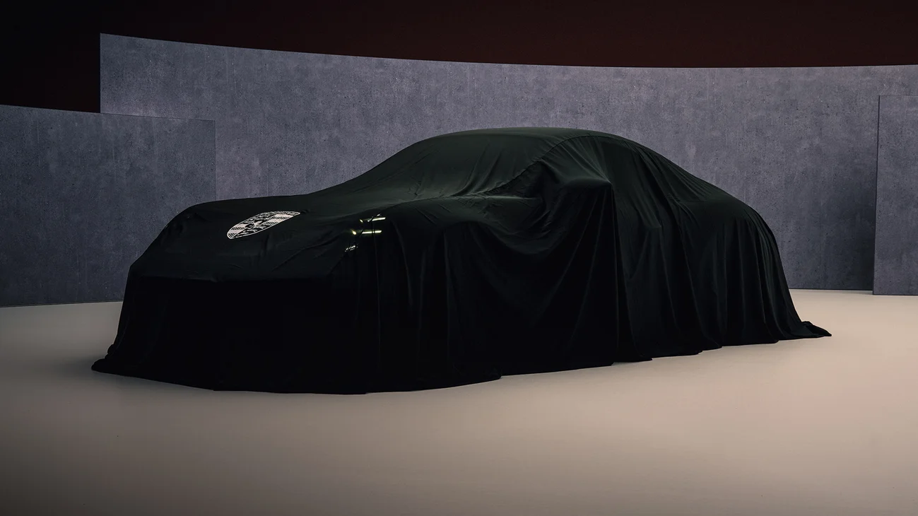 Front shot of a Porsche covered with a black cloth in a studio.