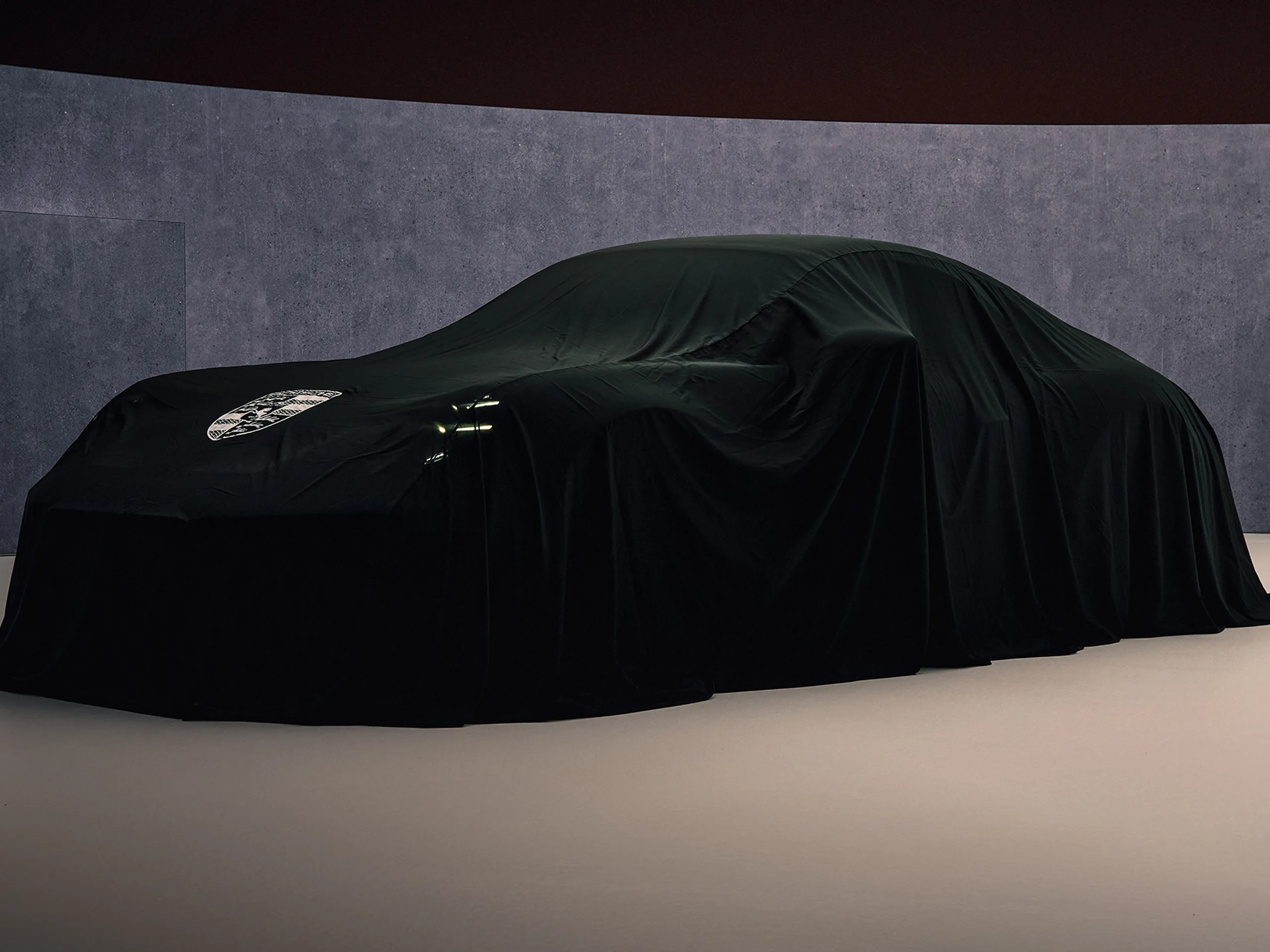 Front shot of a Porsche covered with a black cloth in a studio.