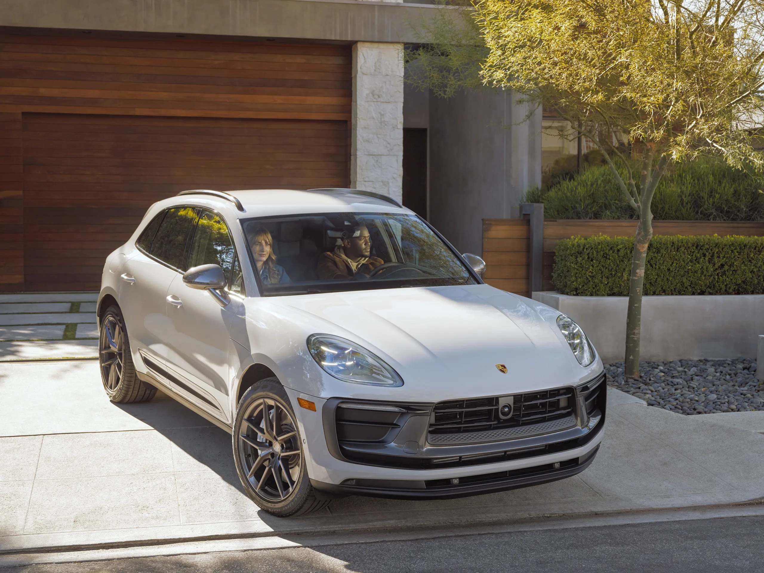 A grey Porsche Macan turning out of a modern home driveway.
