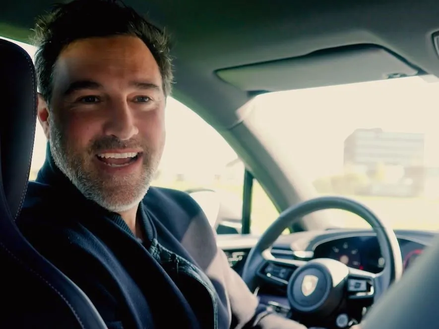 A man sitting inside a Porsche looking at the camera.
