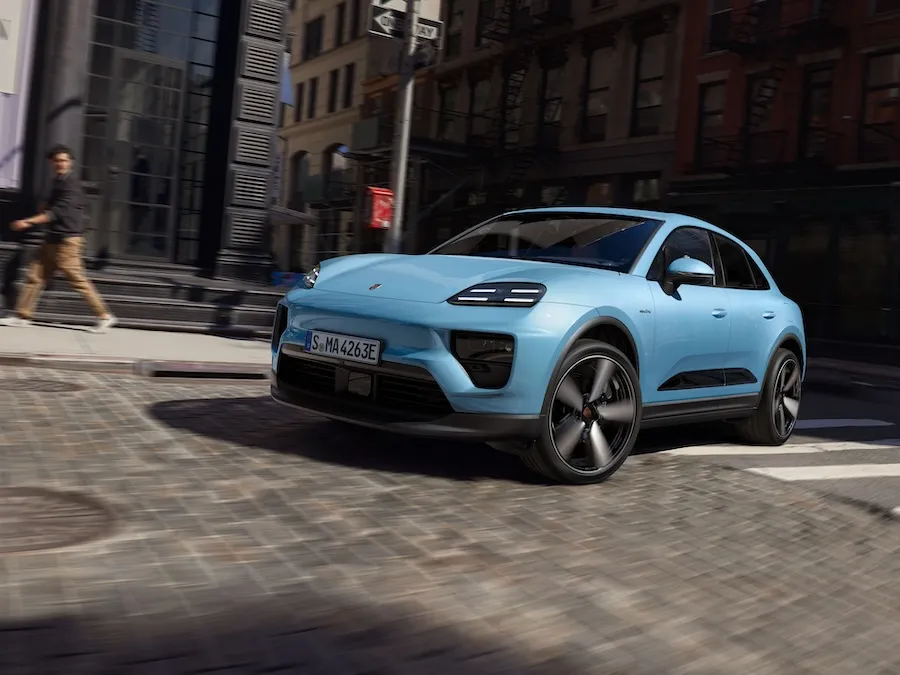 Une Porsche Macan bleu clair qui négocie un virage dans une rue urbaine moderne.