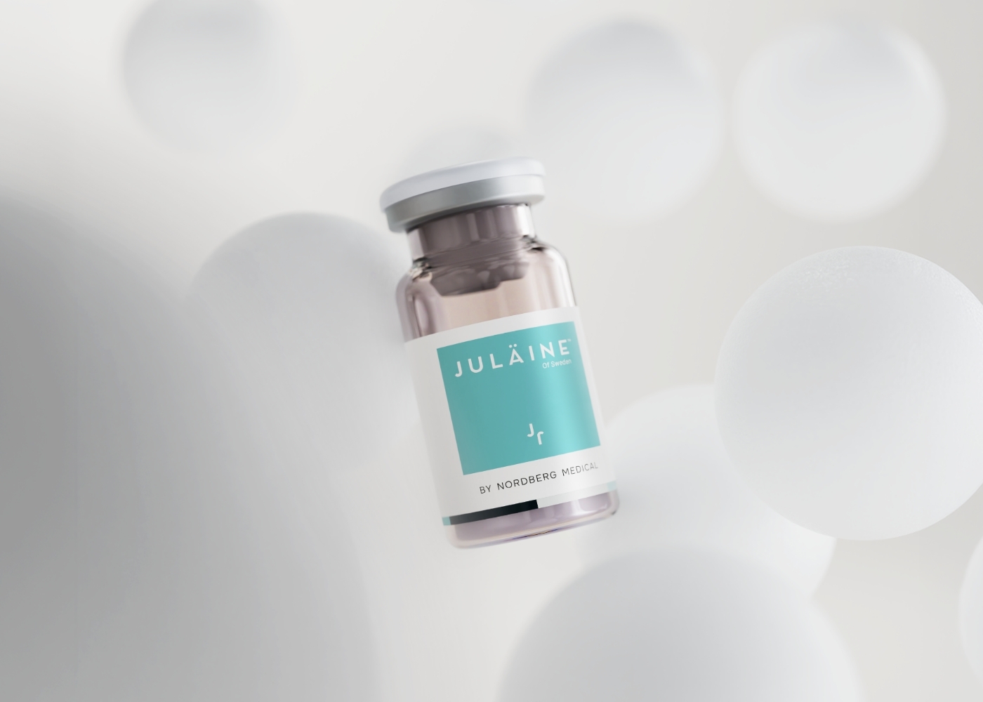 A vial of Juläine by Nordberg Medical on a soft white background surrounded by translucent spheres.
