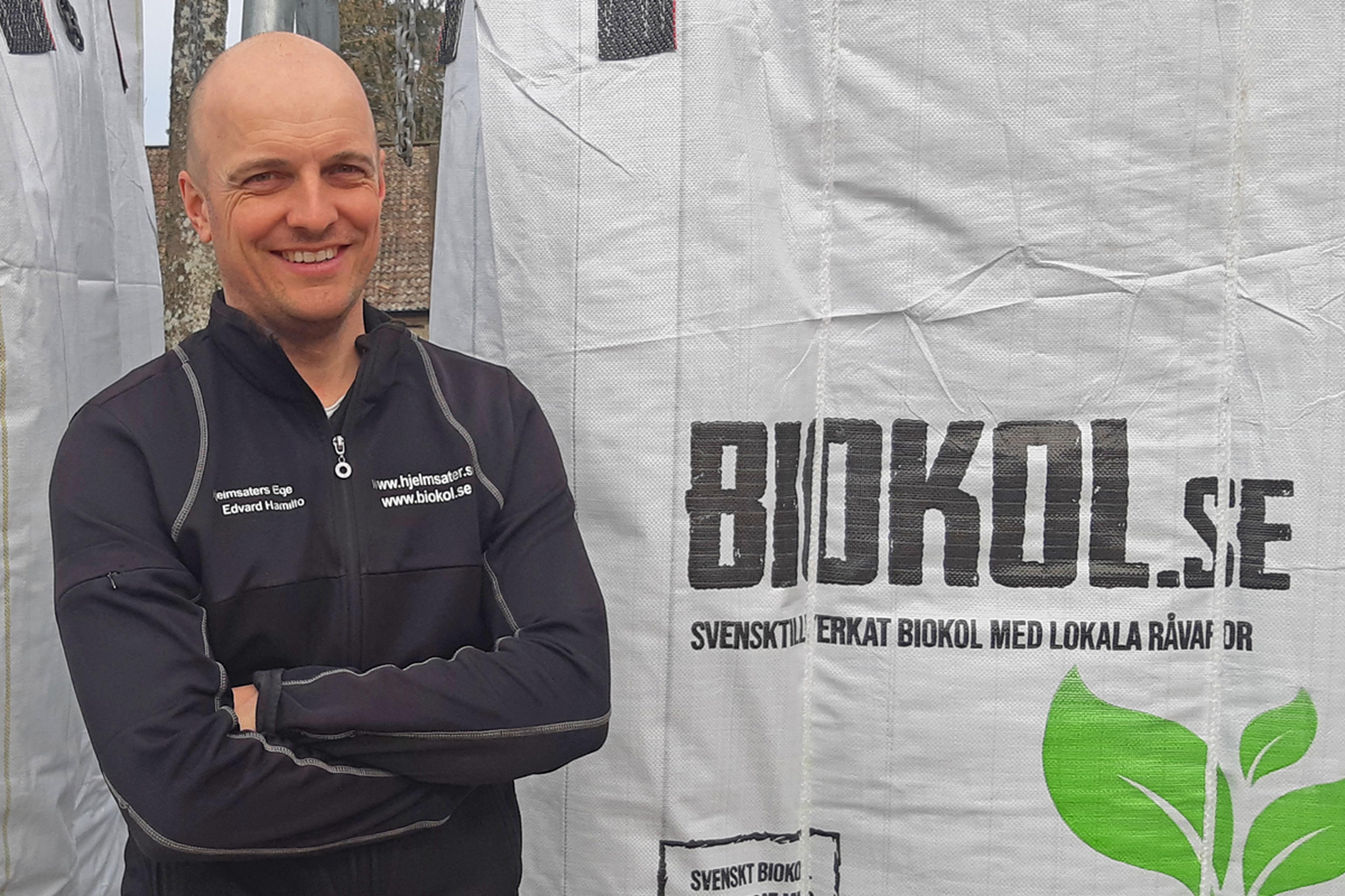 Man in black jacket standing beside large sack labeled "BIOKOL.se" with green leaf logo.