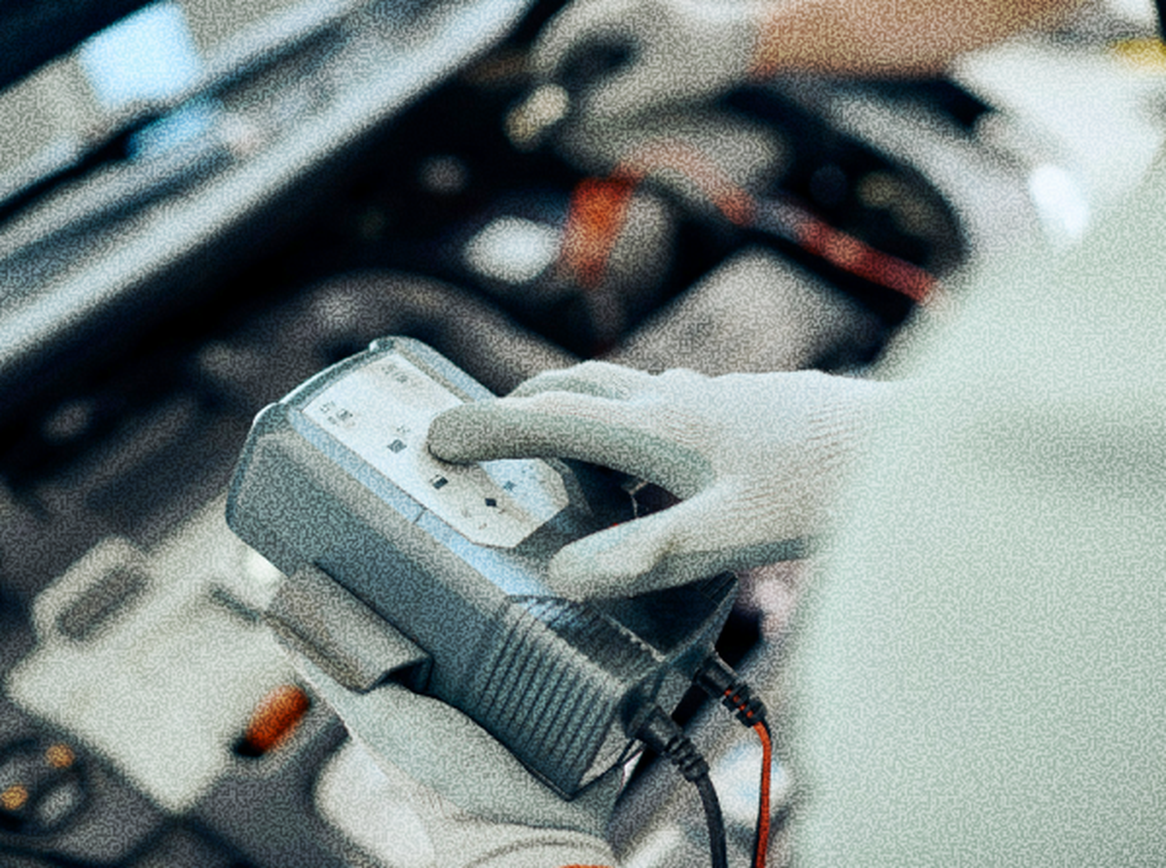 A person wearing gloves holds a diagnostic tool in a car engine bay, suggesting they are checking or repairing the vehicle.