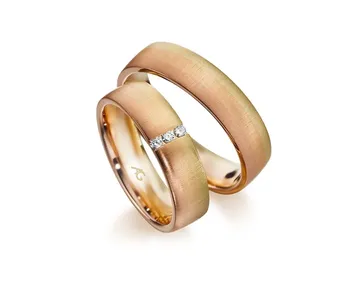 Zwei goldene Eheringe, einer davon mit drei kleinen Diamanten, auf weißem Grund. Die Ringe haben eine glatte, matte Oberfläche.