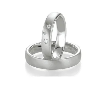 Zwei silberne Eheringe, einer davon mit drei kleinen Diamanten, auf weißem Hintergrund.