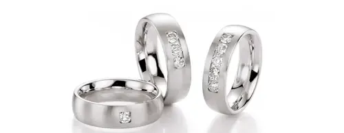 Drei silberne Ringe, zwei stehende und ein liegender, jeweils mit kleinen Diamanten besetzt, auf weißem Hintergrund dargestellt.