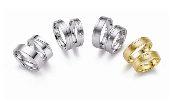 Drei Paar Eheringe in Weißgold und ein Paar Eheringe in Gelbgold, elegant angeordnet auf einem weißen Hintergrund. Die Ringe sind schlicht und modern im Design und enthalten teilweise kleine Zierelemente.