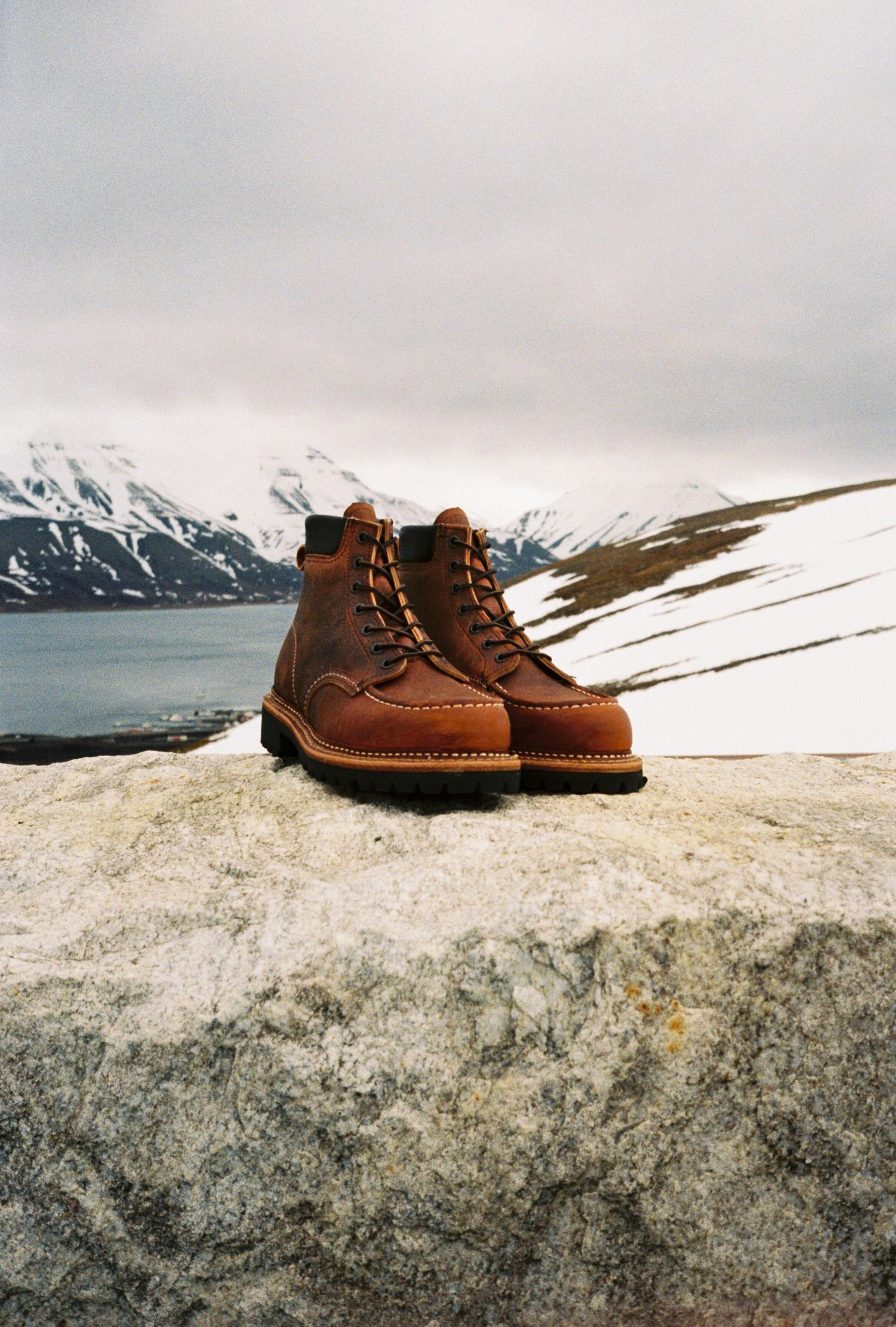 Brown hiking boots on a rock with a snowy mountain landscape in the background.