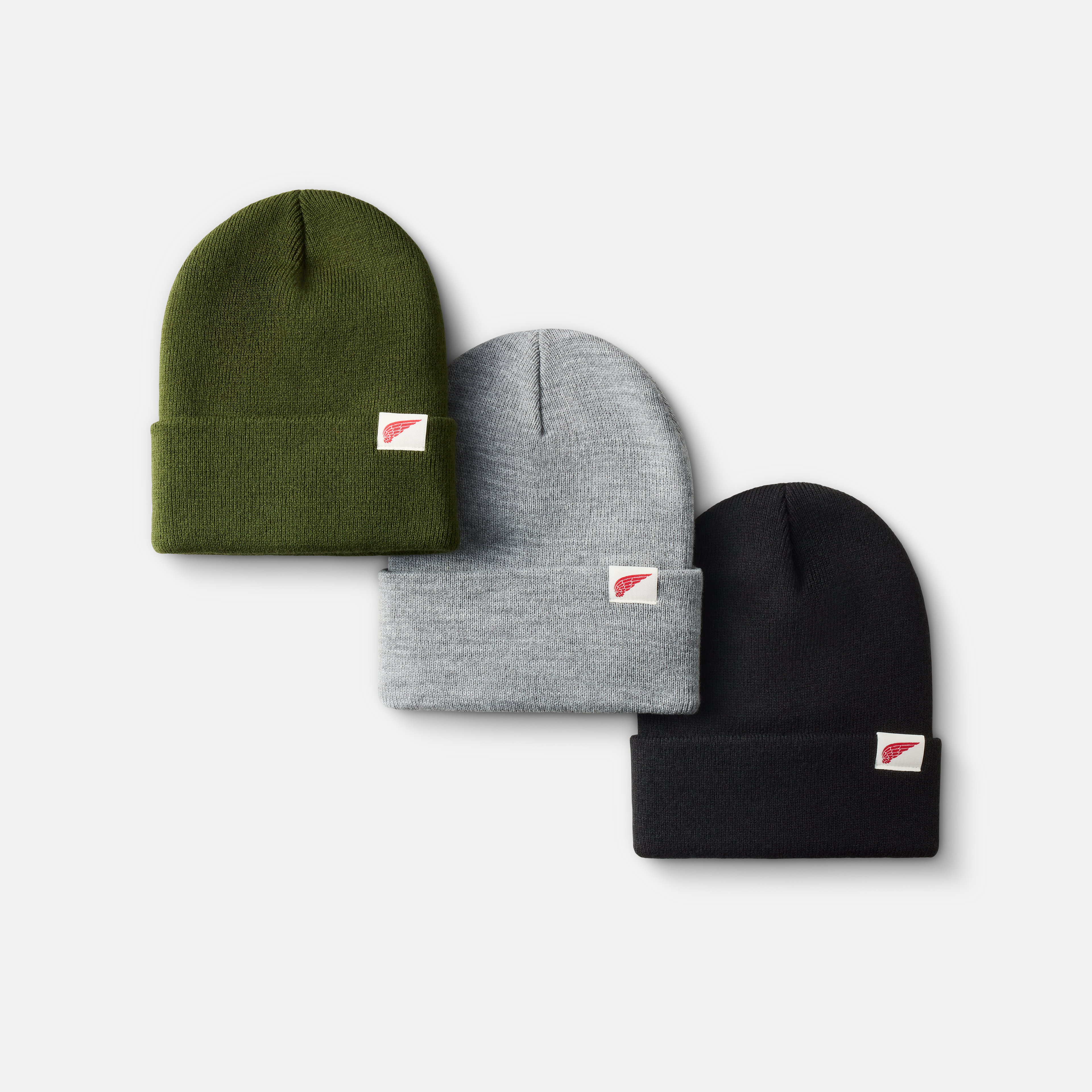 Three folded beanies in olive green, gray, and black with a small red and white logo tag on the front, arranged on a white background.