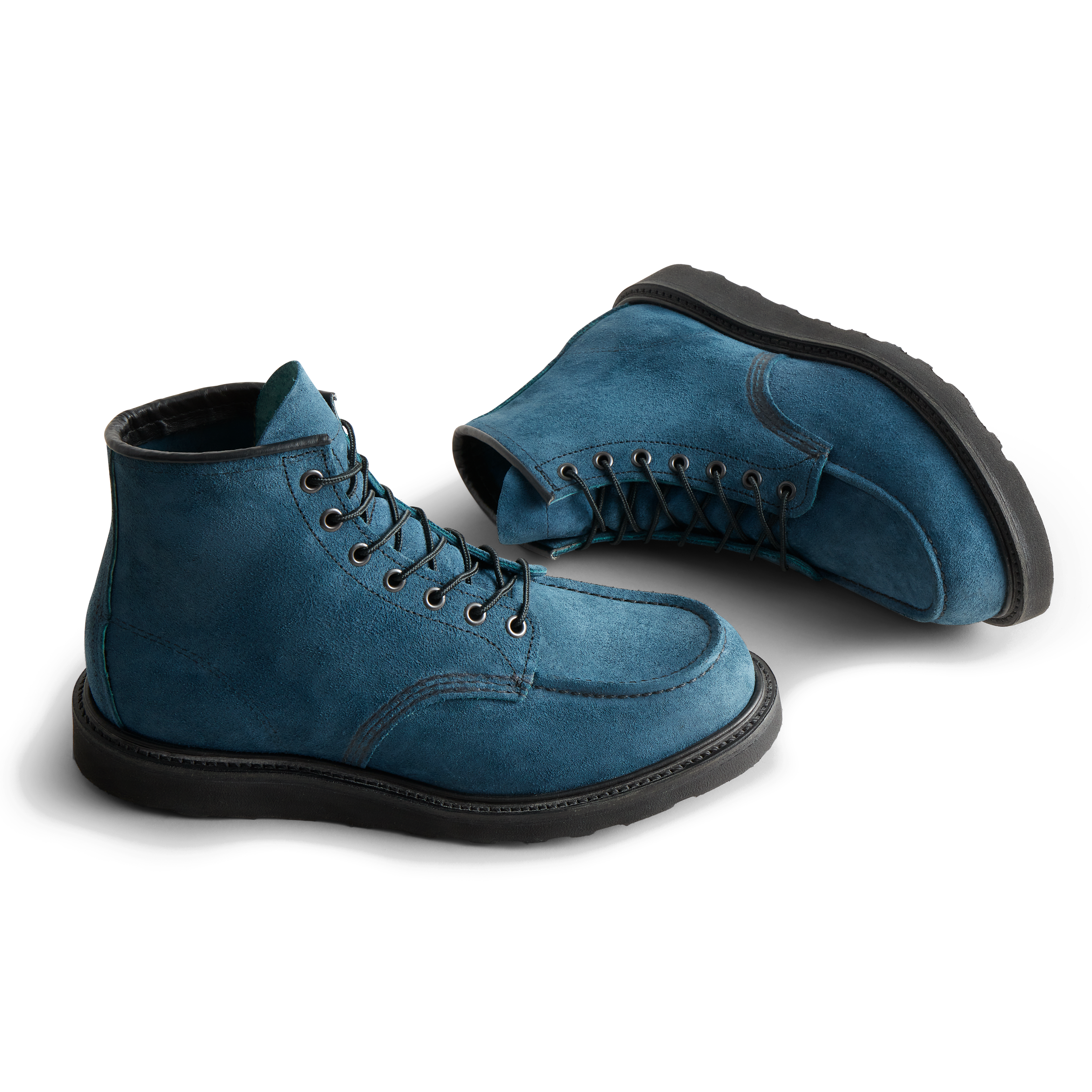 A pair of blue suede boots with black laces and soles, one upright and the other lying on its side, against a white background.