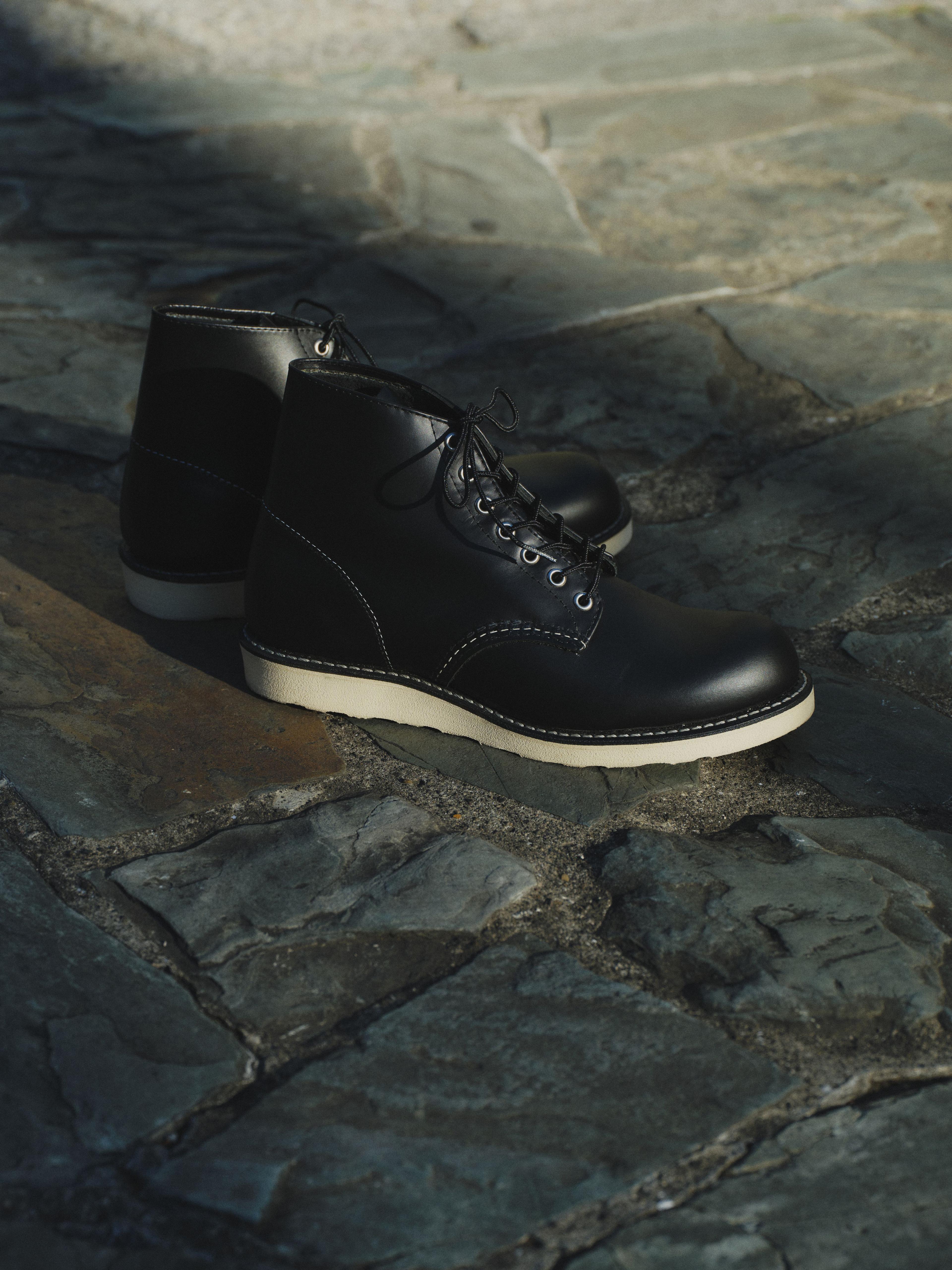 Black leather boots with white soles on a textured stone floor, partially in shadow.