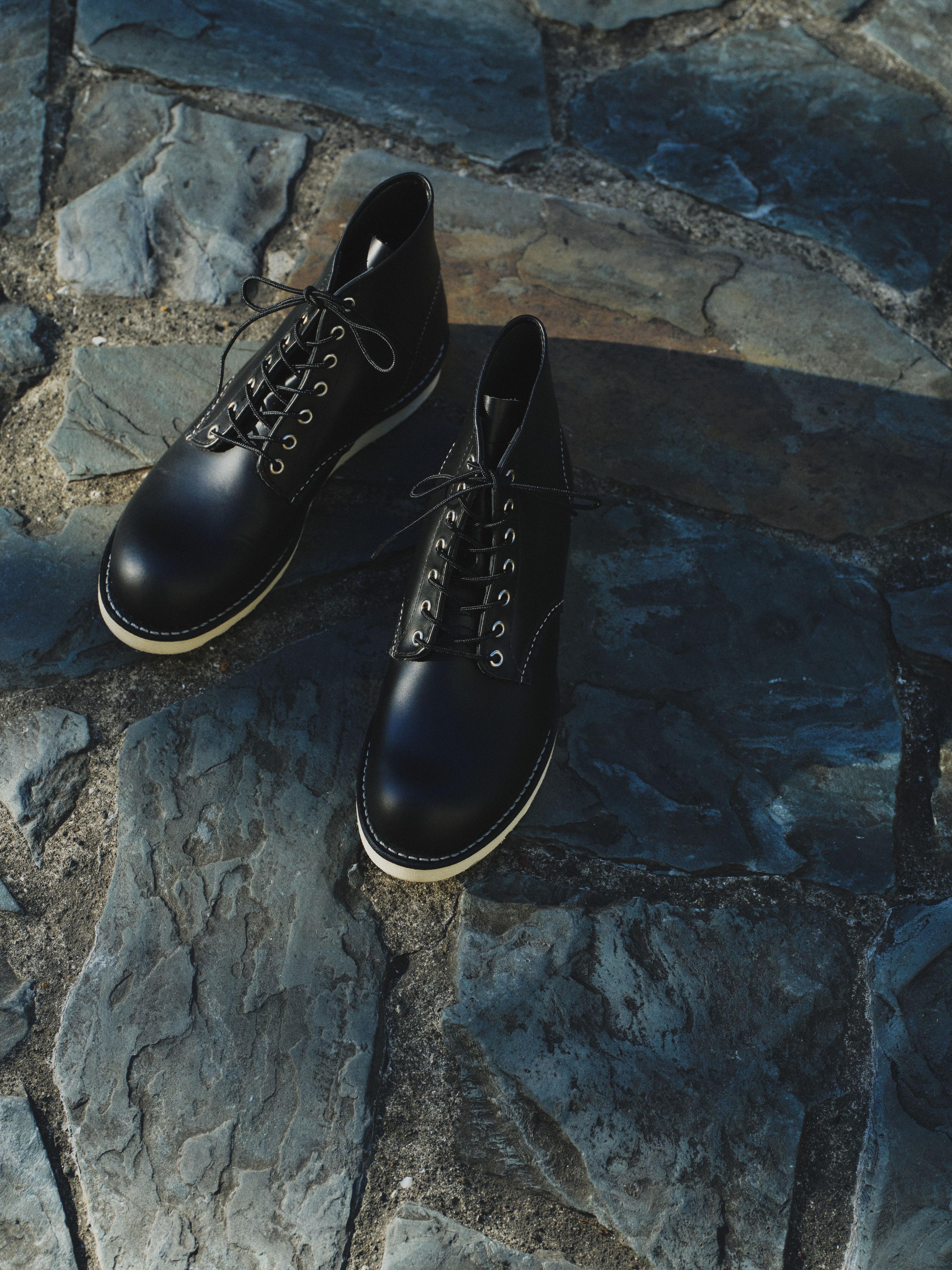 Black leather boots on a textured stone pavement, with laces neatly tied.