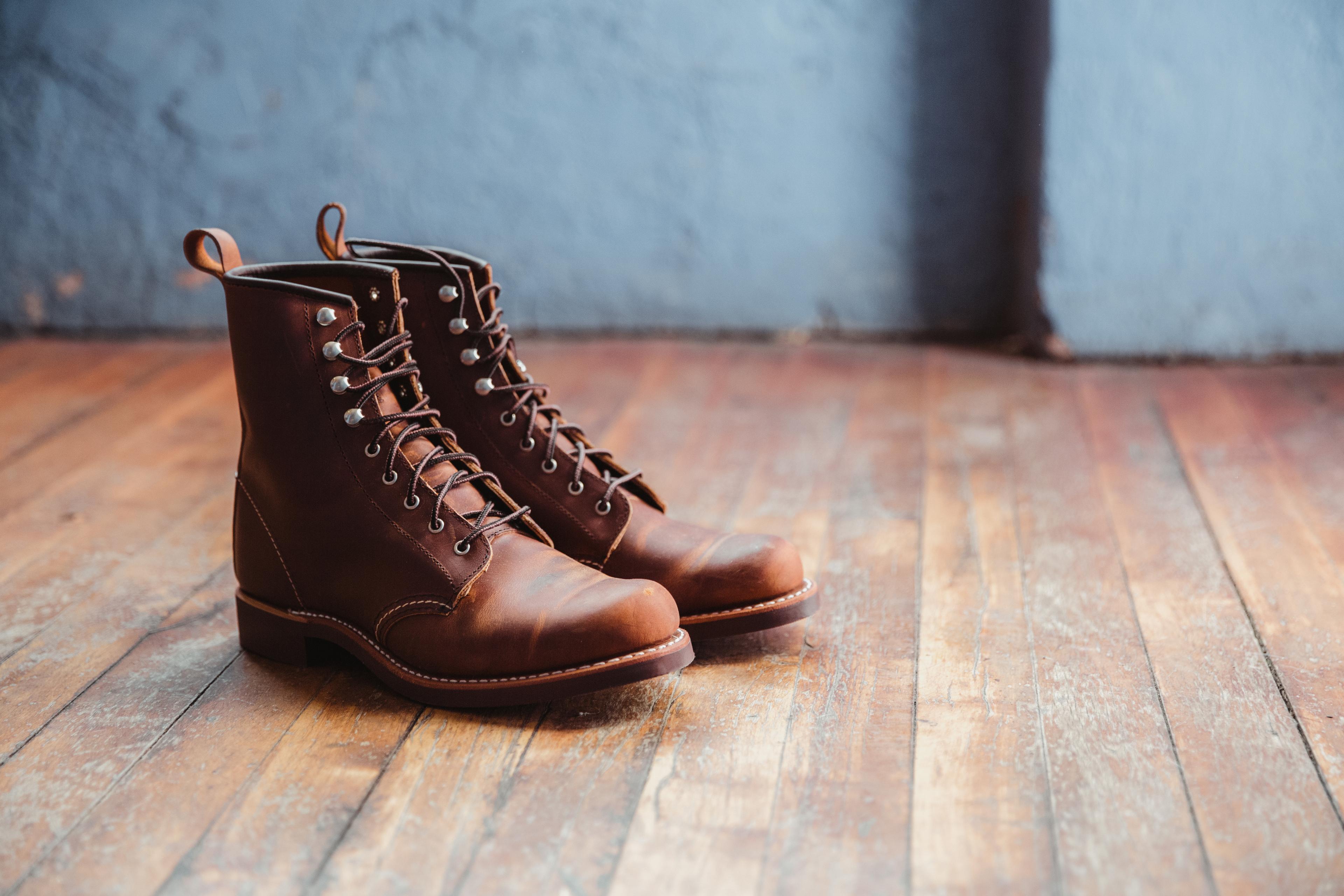A pair of brown leather lace-up boots on a wooden floor, against a blue-gray textured wall.