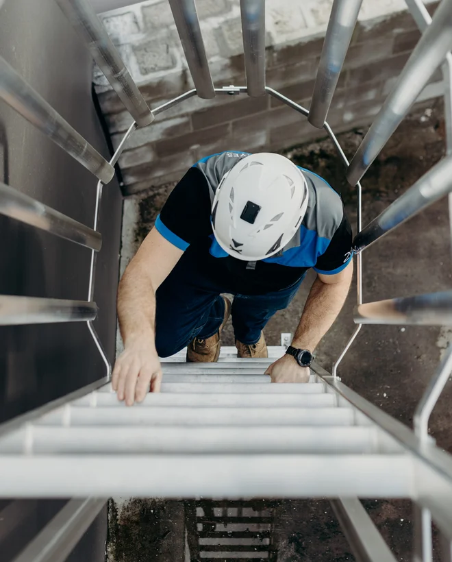Worker in a safety helmet climbing a caged aluminium access ladder