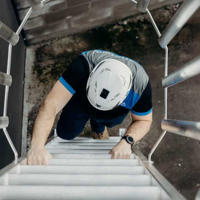 Overhead view of a worker in a helmet climbing an aluminium access ladder