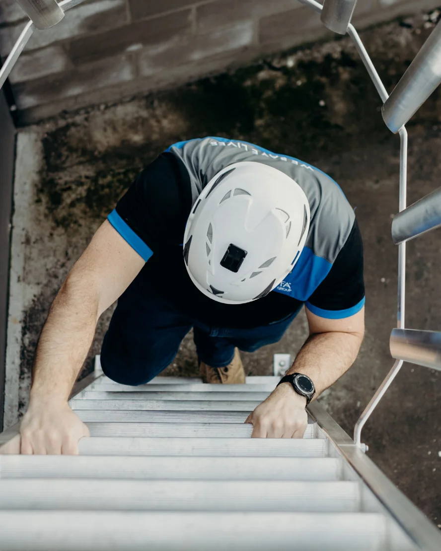 Worker in a helmet climbing a Kattsafe access ladder