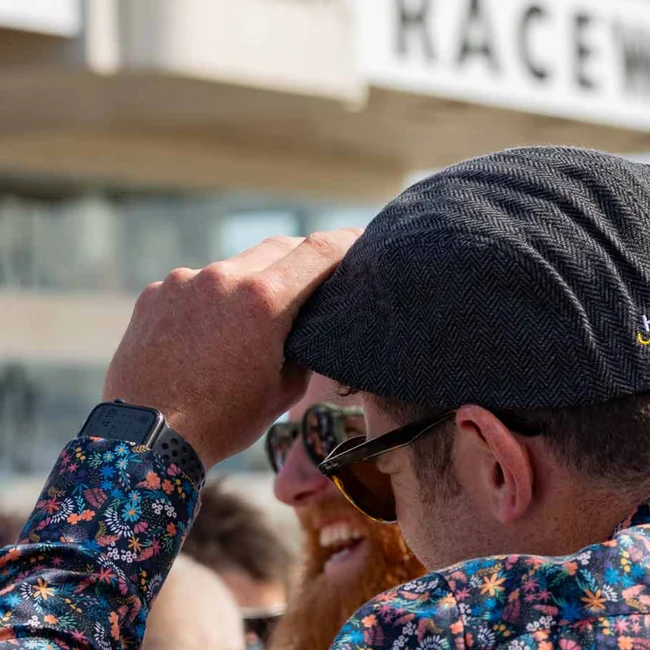 Man in a herringbone flat cap and floral shirt watching the action at a raceway