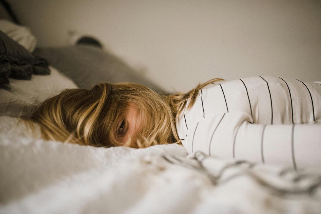 Person lying face down on a bed, wearing a white striped shirt. Their hair is partially covering their face.