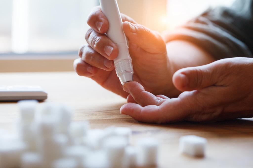 Person using a lancet device to prick their fingertip for a blood sugar test, with sugar cubes blurred in the foreground.