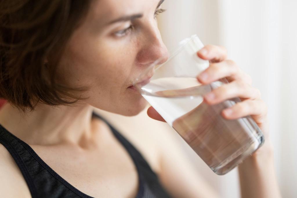 Woman in a black tank top drinking a glass of water, with a focused expression.