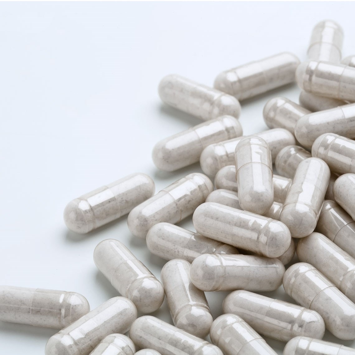 A pile of white capsules scattered on a smooth, light surface. The capsules are glossy and uniformly shaped.