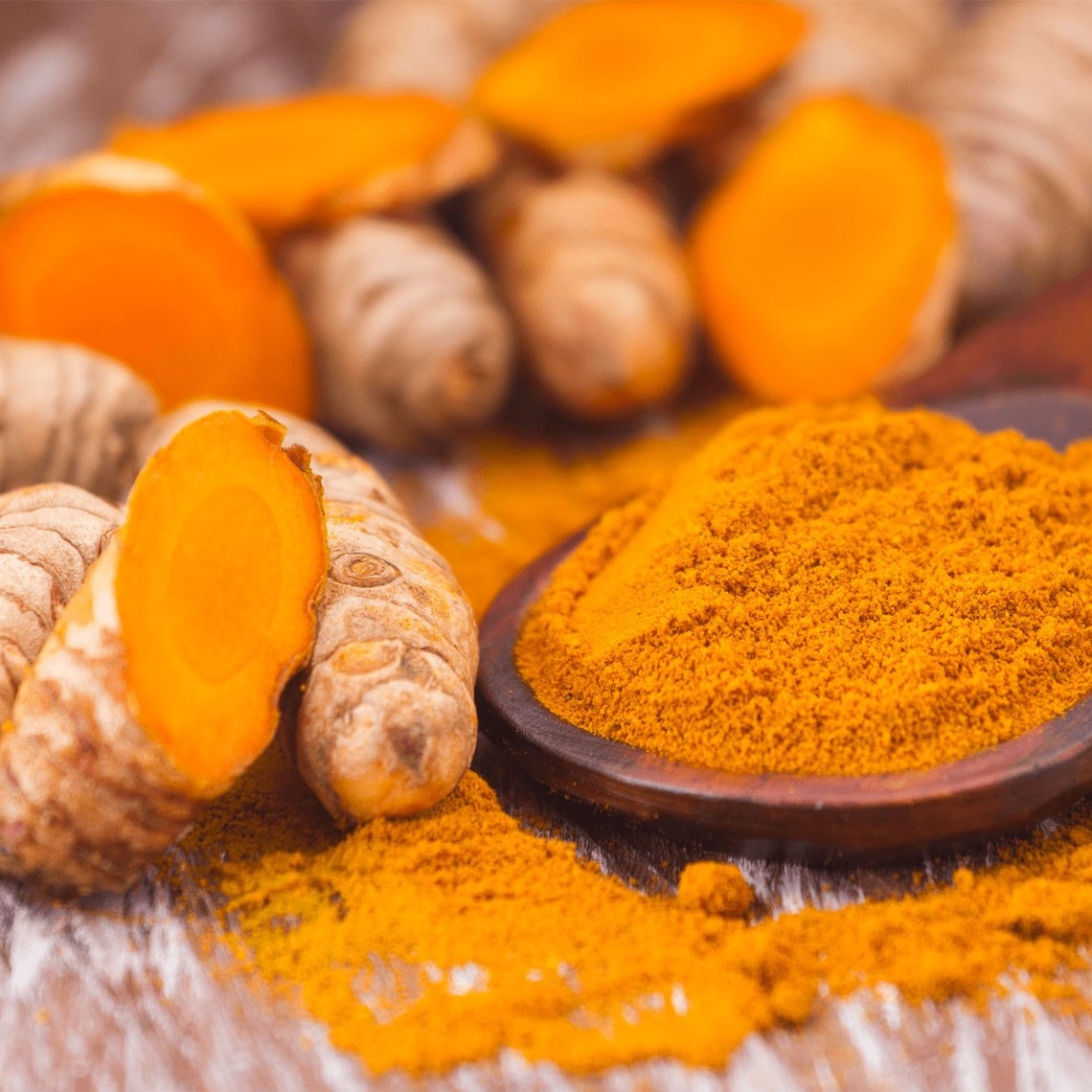 Fresh turmeric roots and a wooden bowl filled with vibrant turmeric powder on a rustic surface.