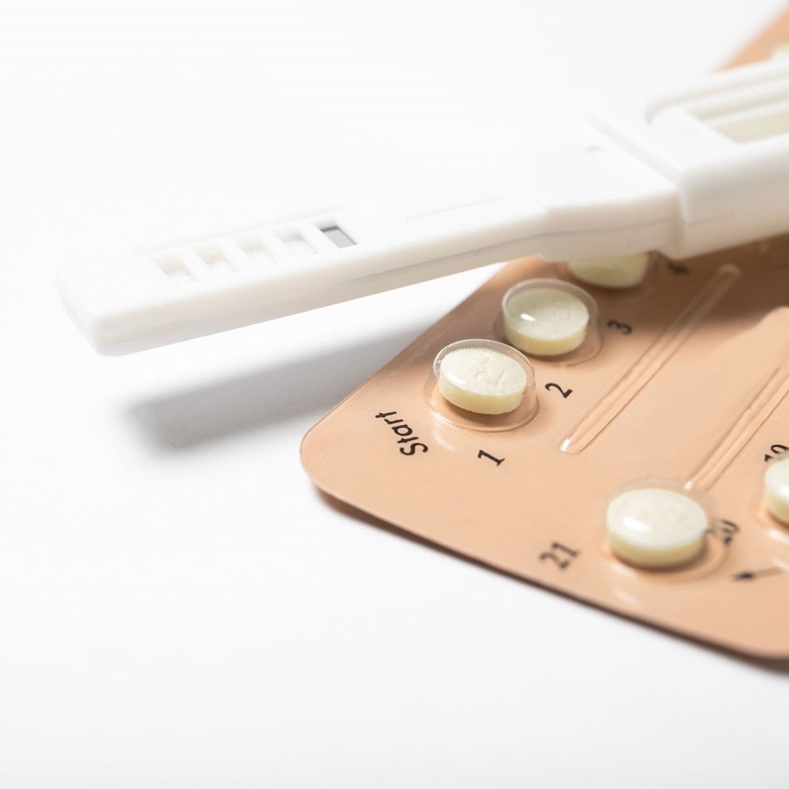 Close-up of a pregnancy test and a blister pack of birth control pills on a white surface.
