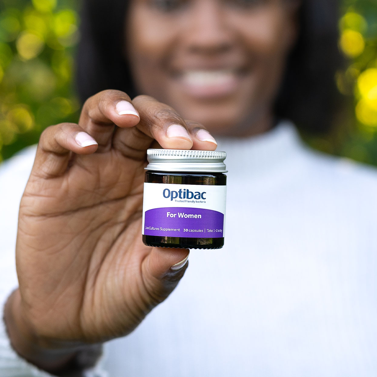 Person holding a small jar of Optibac probiotics for women, with a blurred green background.