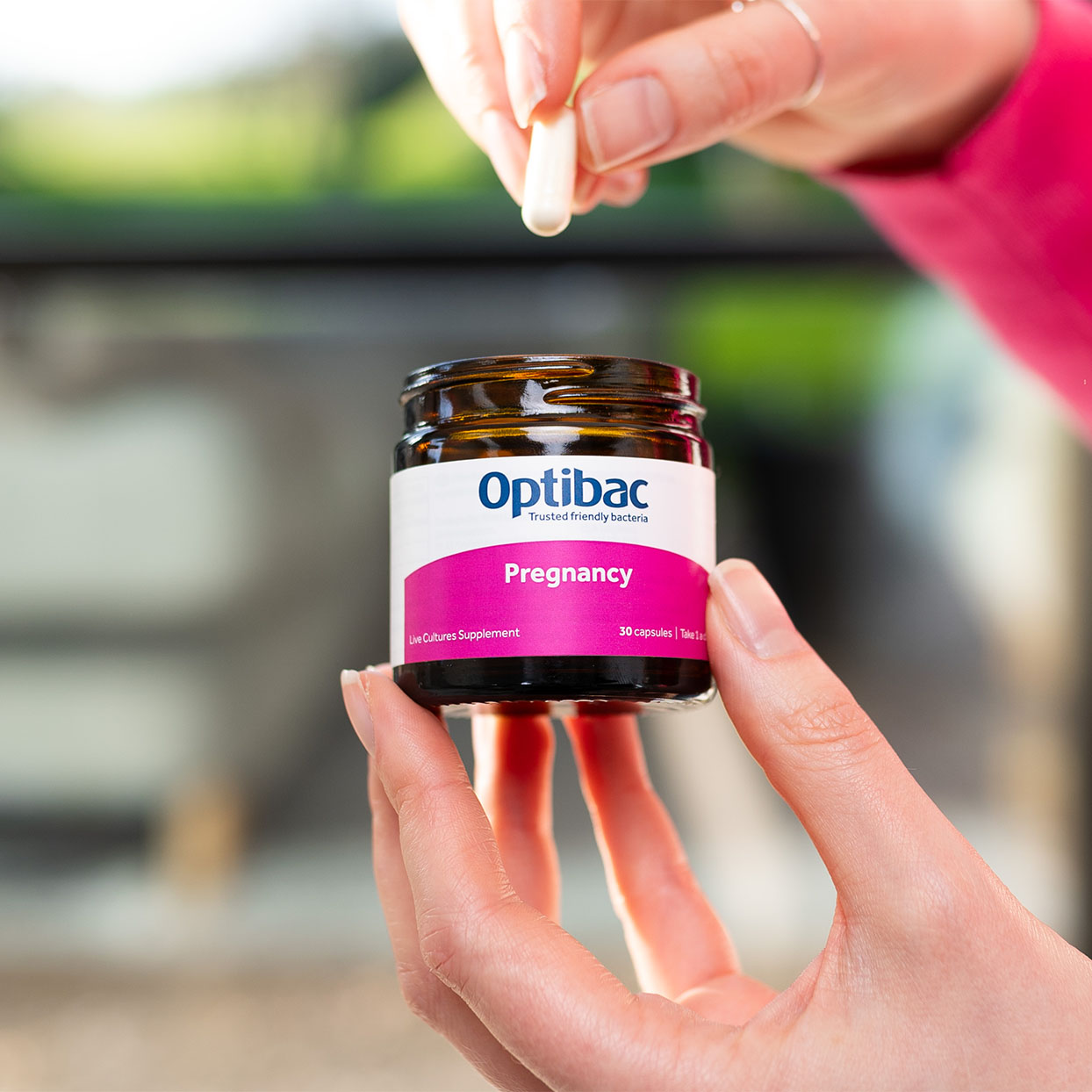 A person holds a capsule above a jar labeled "Optibac Pregnancy," containing 30 live cultures supplements.