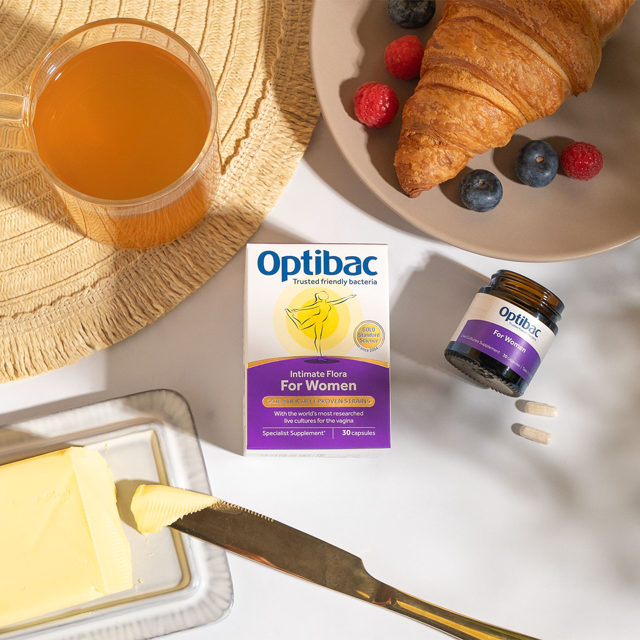 Optibac supplements with a croissant, berries, orange juice, and butter on a table.