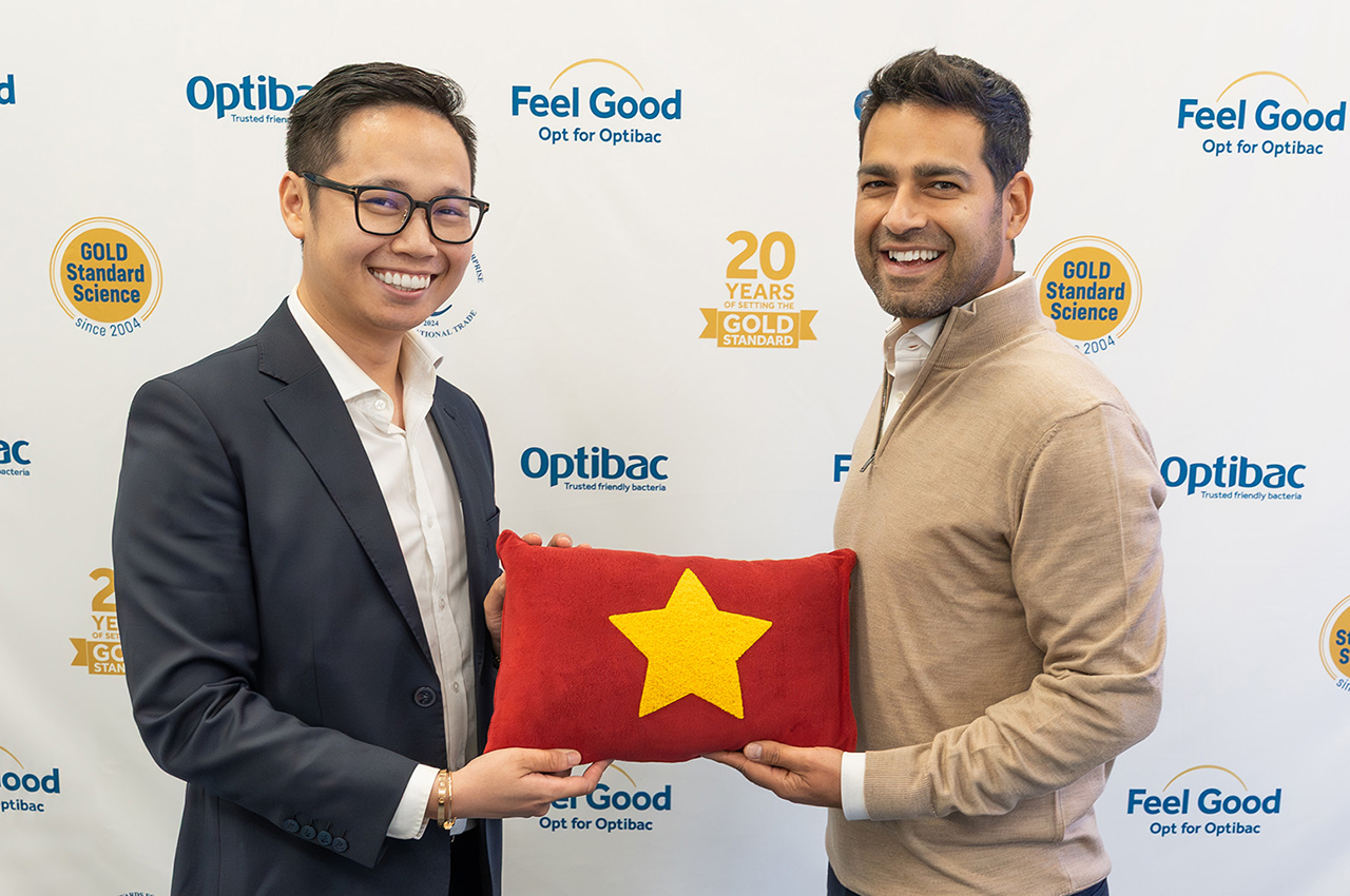 Two men smiling and holding a red pillow with a yellow star, standing in front of a branded backdrop.