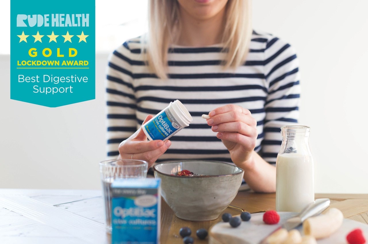 Woman in striped shirt taking a supplement from a bottle at a breakfast table with berries, milk, and a "Best Digestive Support" award badge.