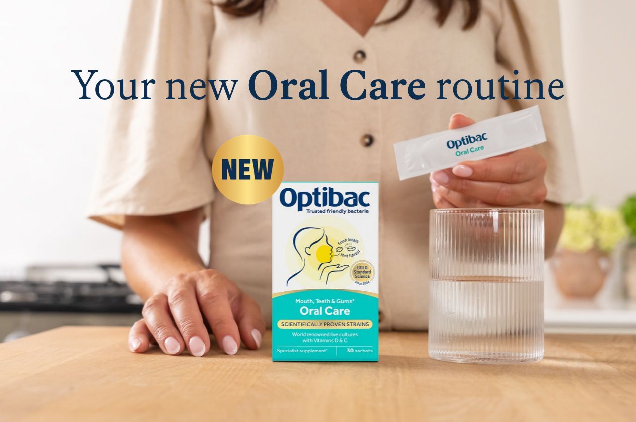 A person holding an Optibac Oral Care sachet next to a glass of water and a box of the product on a wooden table.
