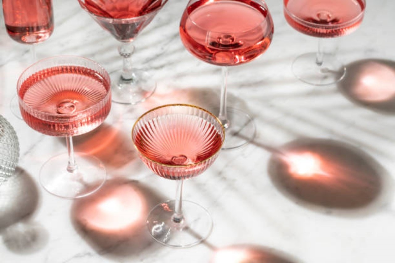Various elegant glasses filled with pink rosé wine casting shadows on a white marble surface.