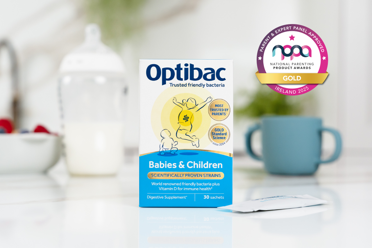 Optibac probiotics box for babies and children on a table with a parenting award badge, surrounded by a cup, milk jug, and berries.