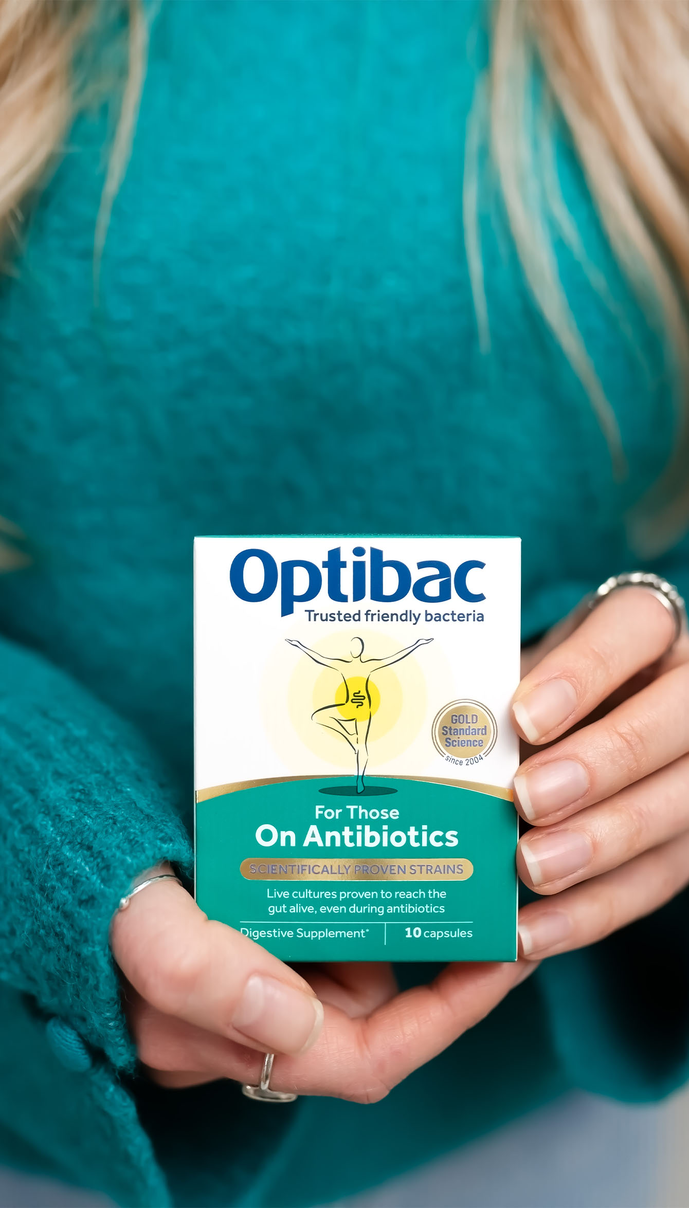 Person in teal sweater holding a box of Optibac probiotics for antibiotic use, featuring a gold award emblem and 10 capsules.