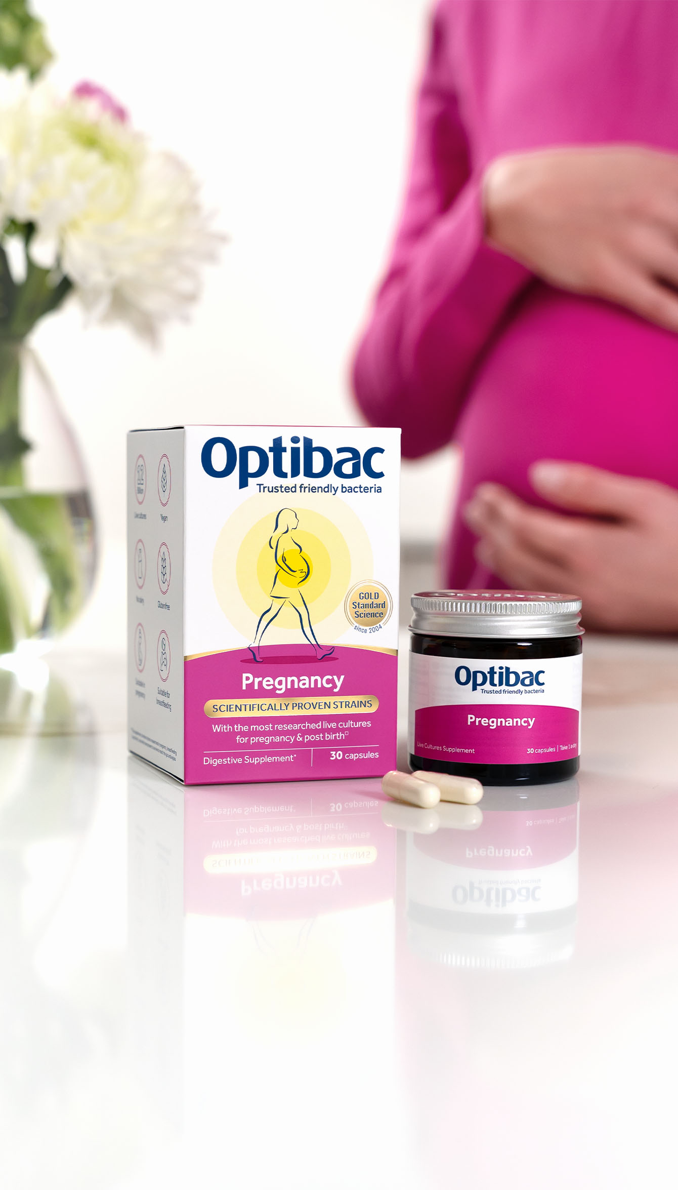 Optibac Pregnancy probiotics on a table with a pregnant person in pink and flowers in the background.