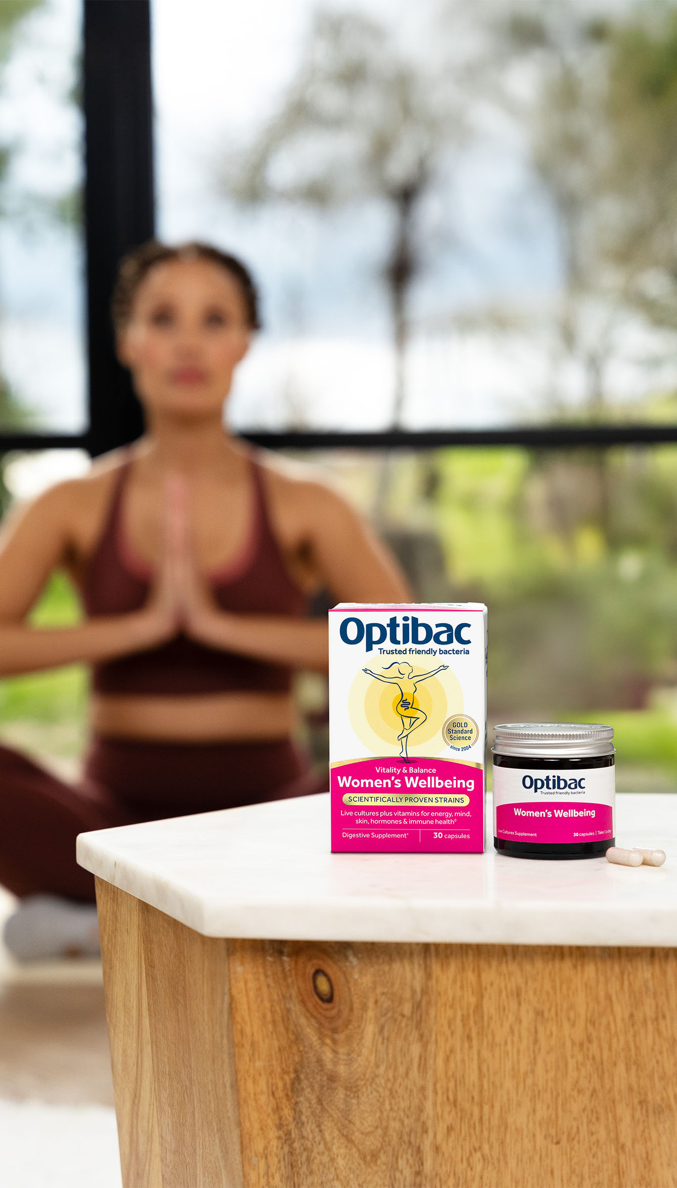 Optibac probiotics on a table with a woman in workout attire meditating in the background.