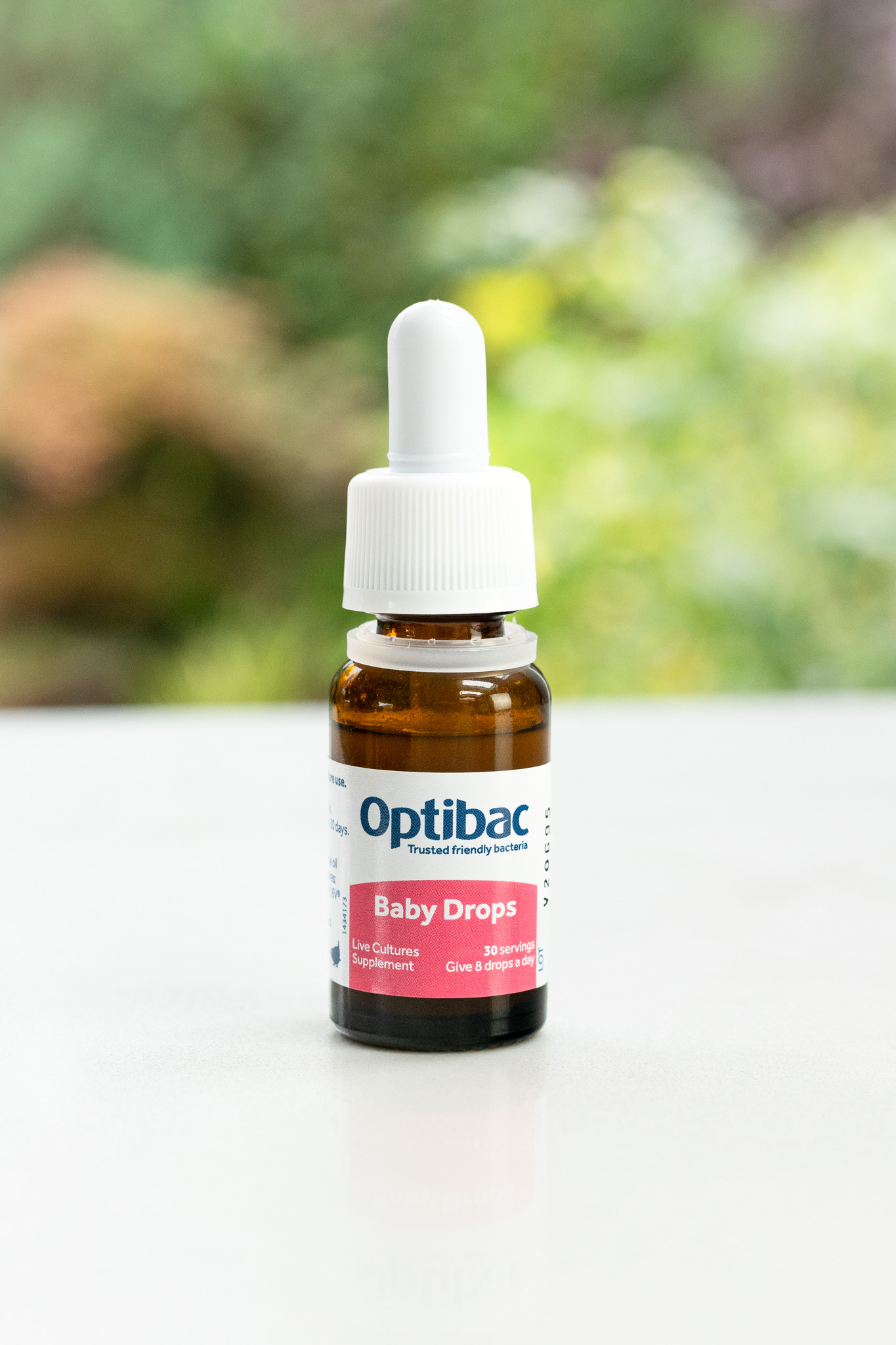 Optibac Baby Drops bottle on a white surface with a blurred green background.