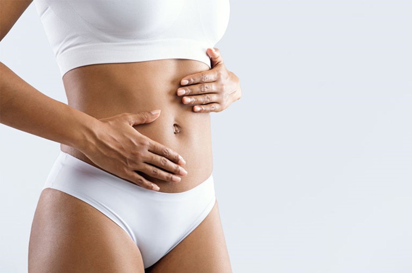 Person in white underwear touching their abdomen, suggesting focus on stomach health or digestion, against a light gray background.