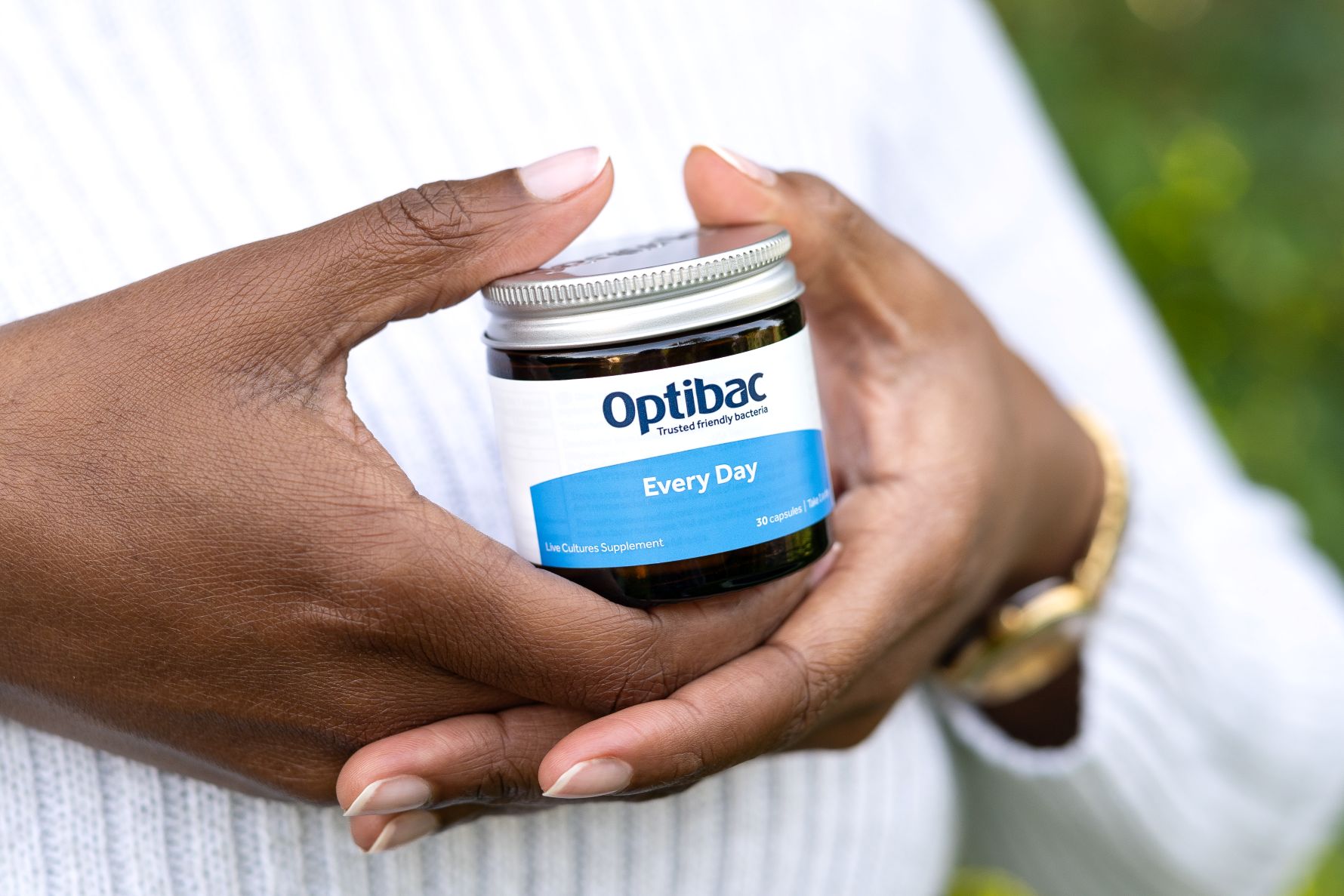 Hands holding a jar of Optibac "Every Day" live cultures supplement against a blurred background.