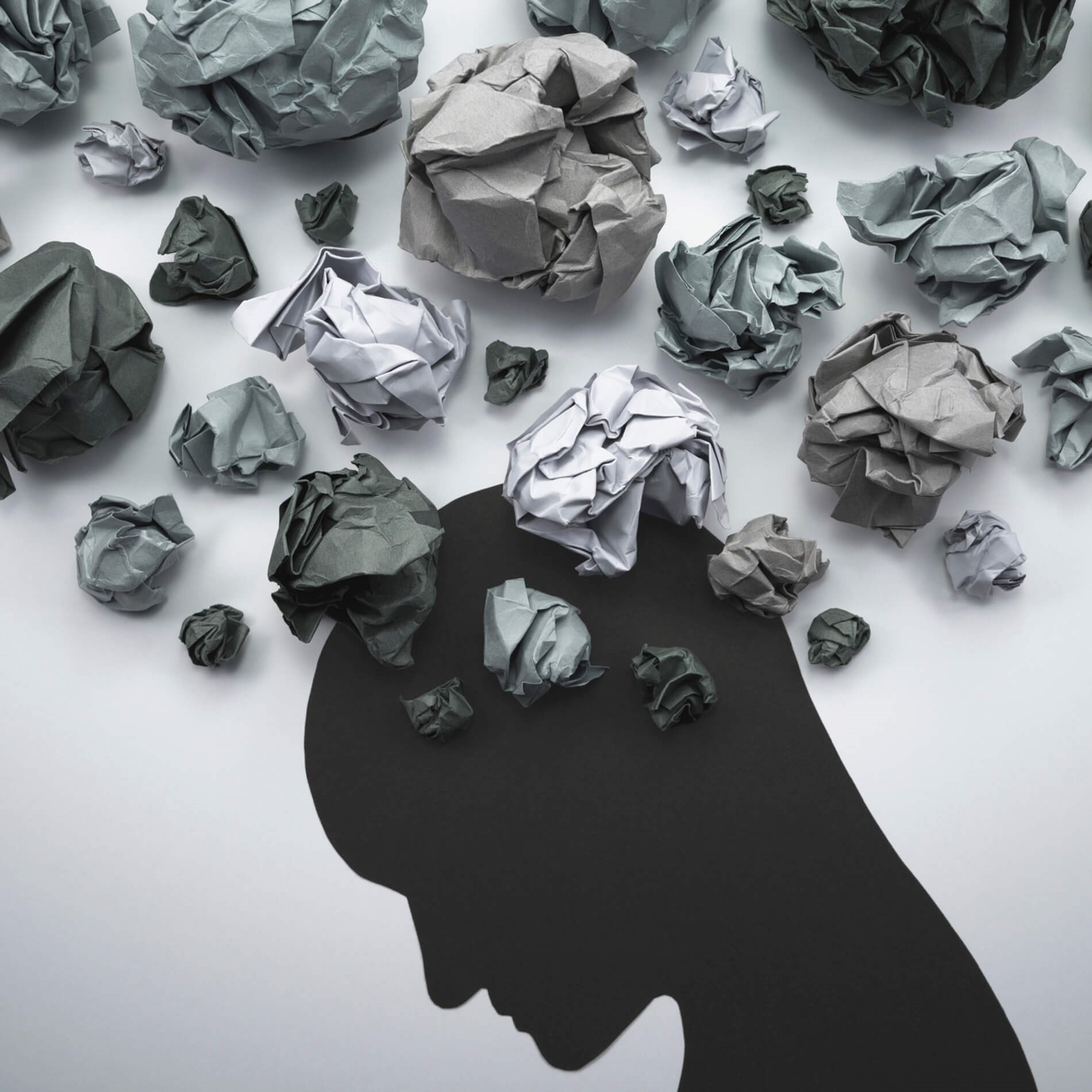 Silhouette of a person with crumpled paper balls above, symbolizing thoughts or stress.