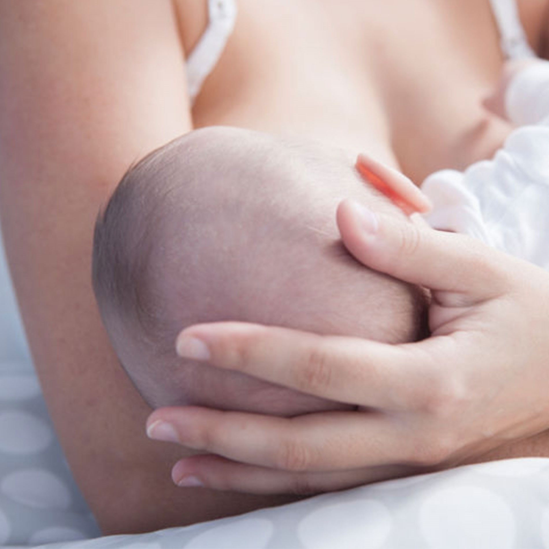 A person breastfeeding an infant, cradling the baby's head gently in their hand, with a soft-focus background.