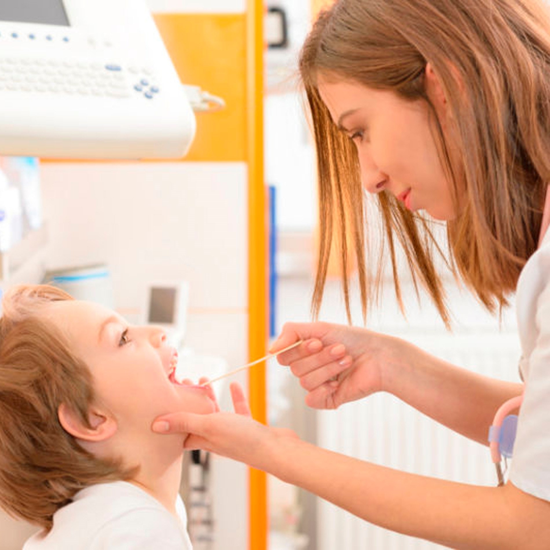 A dentist examines a young boy's mouth using a tongue depressor in a bright dental clinic.